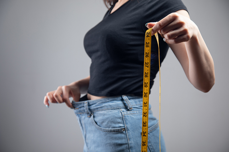 Weight loss and a healthy diet – a woman holding loose jeans after a weight loss program.