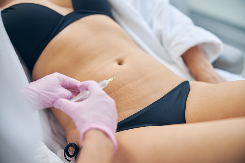 A cosmetologist performing a lipolytic injection treatment on the abdominal area to reduce localized fat deposits.